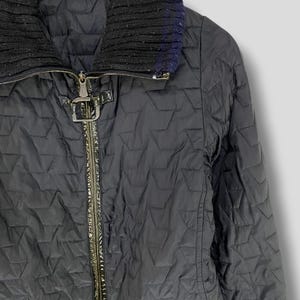 May include: Black quilted jacket with a zipper closure and a black knit collar. The jacket has a green patent leather trim and a silver buckle detail.