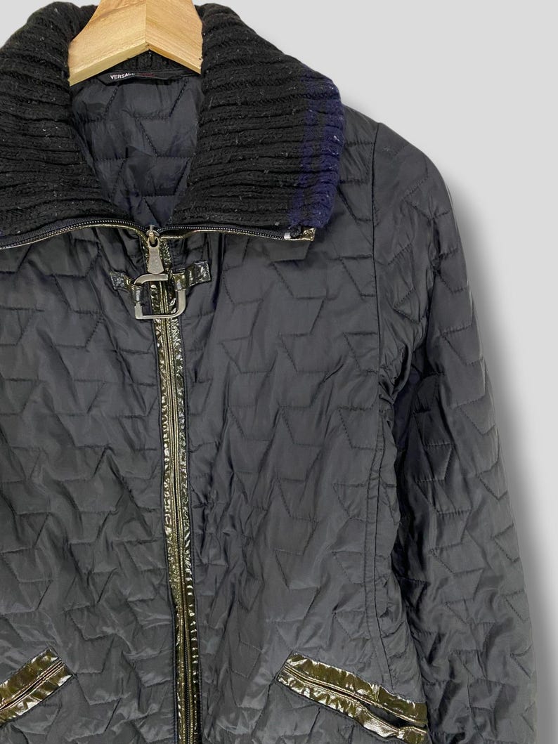 May include: Black quilted jacket with a zipper closure and a black knit collar. The jacket has a green patent leather trim and a silver buckle detail.