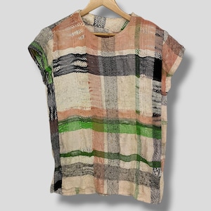 May include: A short-sleeved top with a plaid pattern in beige, peach, green, black, and gray. The shirt is hanging on a wooden hanger against a light gray background. The fabric appears to be woven.