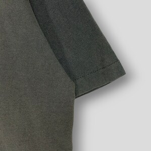 May include: Close-up of a dark gray t-shirt sleeve. The fabric has a textured appearance, and the sleeve's edge is neatly hemmed with visible stitching. The shirt appears to be made of a soft, comfortable material.