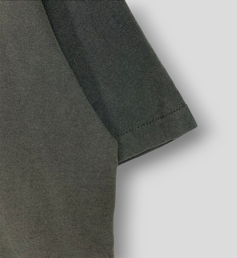 May include: Close-up of a dark gray t-shirt sleeve. The fabric has a textured appearance, and the sleeve's edge is neatly hemmed with visible stitching. The shirt appears to be made of a soft, comfortable material.