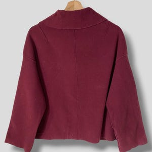 Puede incluir: Un su&eacute;ter burdeos con cuello alto y doblado y mangas largas. El su&eacute;ter tiene un corte holgado y una longitud ligeramente recortada.