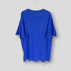 May include: A vibrant royal blue t-shirt with short sleeves, suspended against a white backdrop. The shirt features a crew neck and is likely crafted from a soft fabric. There are a few small, light-coloured marks on the front of the shirt.