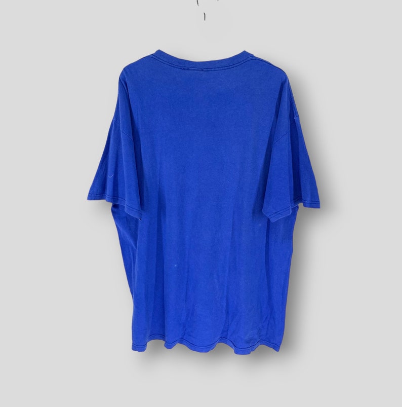 May include: A vibrant royal blue t-shirt with short sleeves, suspended against a white backdrop. The shirt features a crew neck and is likely crafted from a soft fabric. There are a few small, light-coloured marks on the front of the shirt.