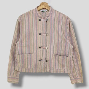 Pode incluir: Casaco listrado multicolorido com gola mandarim e dois bolsos frontais. O casaco tem três fechos de alternância de metal e está pendurado em um cabide de madeira. A etiqueta diz "SIMPLELIFE".