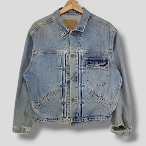 May include: Light blue denim jacket with a button-up front, two chest pockets, and two side pockets. The jacket has a classic collar and long sleeves. The denim has a faded, worn look.