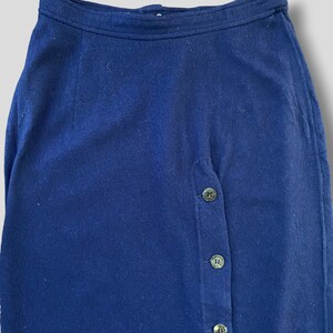 Puede incluir: Falda azul marino con cierre de botones. La falda est&aacute; hecha de una tela suave y presenta una cintura alta. Los botones son de un color oscuro y apagado. La falda es de estilo cl&aacute;sico.