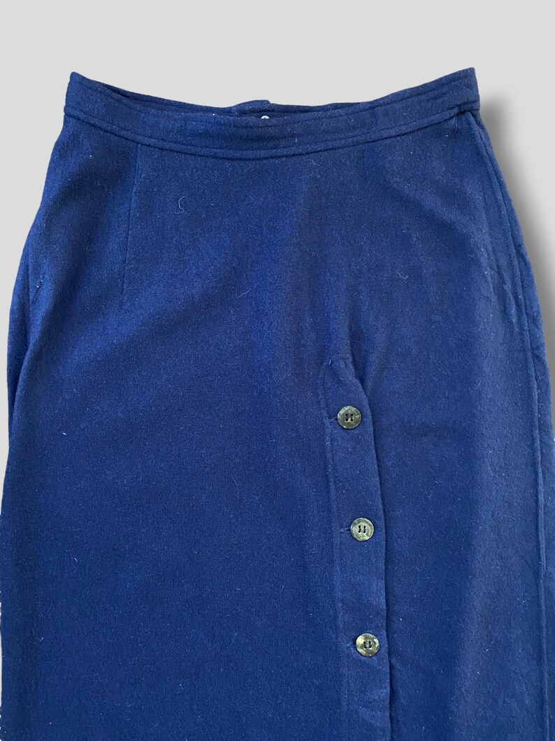 Puede incluir: Falda azul marino con cierre de botones. La falda est&aacute; hecha de una tela suave y presenta una cintura alta. Los botones son de un color oscuro y apagado. La falda es de estilo cl&aacute;sico.