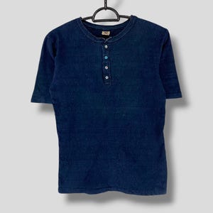 Può includere: Una maglietta blu scuro a maniche corte con colletto abbottonato e quattro bottoni sul davanti.