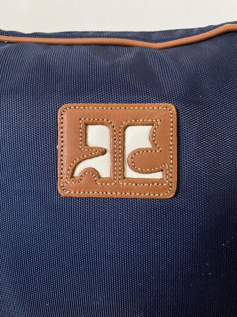 May include: A navy blue bag with a brown leather patch. The patch has a white interior with a brown border and stitched detailing. The bag has a brown trim along the top edge.