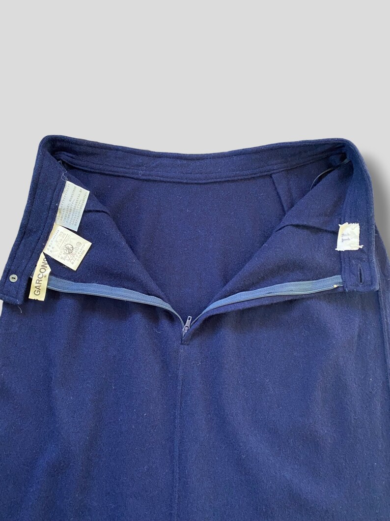 Puede incluir: Falda azul marino con cremallera y bot&oacute;n visibles. La falda tiene un corte recto y un dise&ntilde;o sencillo. La etiqueta de la marca "GARCON" es visible en el lado izquierdo de la cintura. La falda est&aacute; hecha de una tela suave, posiblemente de lana.