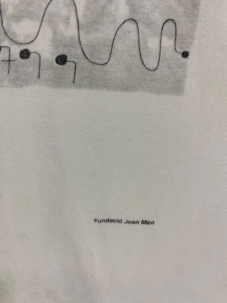 Puede incluir: Tela blanca con un dise&ntilde;o abstracto negro en la parte superior, que incluye l&iacute;neas curvas y puntos. El texto "Fundaci&oacute; Joan Miro" est&aacute; impreso en negro en la parte inferior.