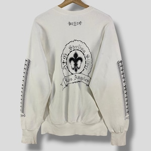 Puede incluir: Sudadera de color crema con gráficos negros. La parte trasera presenta un diseño circular con una flor de lis y las palabras "Sterling Silver Los Angeles". Líneas verticales negras adornan las mangas.