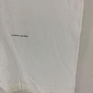 Puede incluir: Una camiseta blanca con el texto "Fundaci&oacute; Joan Mir&oacute;" impreso en negro. La tela tiene una textura sutil. El dobladillo inferior de la camiseta es visible.