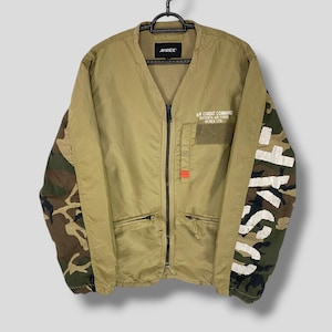 May include: A beige jacket with a zip fastening and camouflage sleeves. The jacket has a V-neck and the text "AIR COMBAT COMMAND" and "AVIREX LTD." is printed on the front.