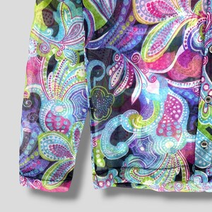 Puede incluir: Una blusa transparente de manga larga con un vibrante estampado de cachemira en tonos azules, morados, rosas y verdes. La tela es ligera y semitransparente, con botones en la parte delantera. El dise&ntilde;o presenta formas florales y abstractas.