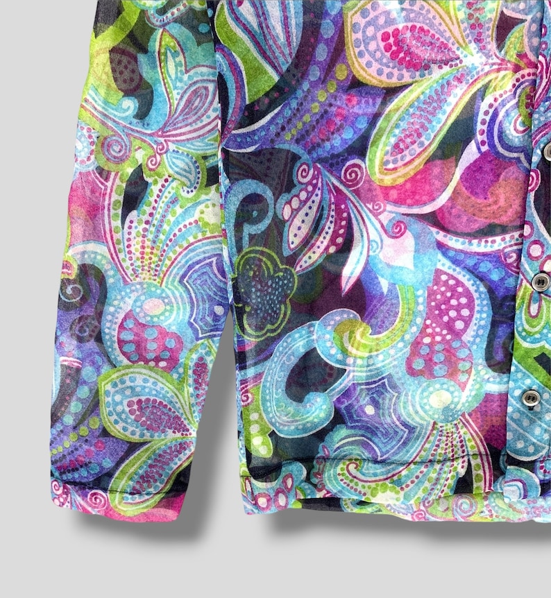 Puede incluir: Una blusa transparente de manga larga con un vibrante estampado de cachemira en tonos azules, morados, rosas y verdes. La tela es ligera y semitransparente, con botones en la parte delantera. El dise&ntilde;o presenta formas florales y abstractas.