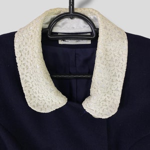 Puede incluir: Una chaqueta azul marino con cuello de encaje blanco. La chaqueta tiene dos botones grandes en la parte delantera y una etiqueta que dice "A.L.C. Par&iacute;s".