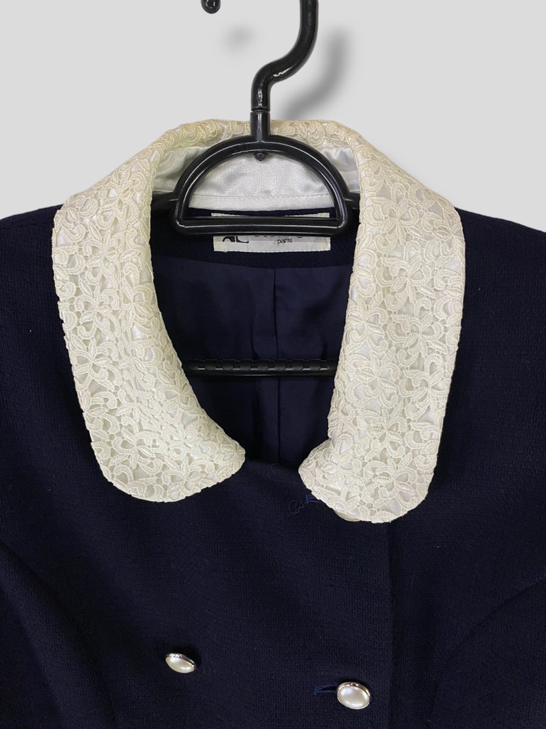 Puede incluir: Una chaqueta azul marino con cuello de encaje blanco. La chaqueta tiene dos botones grandes en la parte delantera y una etiqueta que dice "A.L.C. Par&iacute;s".