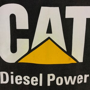 May include: Black background with the white word "CAT" above a yellow triangle. Below the triangle, the words "Diesel Power" are printed in white. The image is a close-up of a logo.