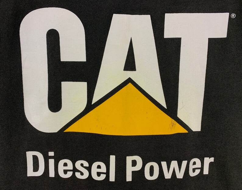 May include: Black background with the white word "CAT" above a yellow triangle. Below the triangle, the words "Diesel Power" are printed in white. The image is a close-up of a logo.