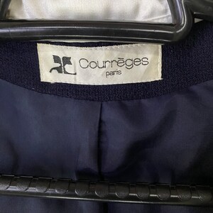 Puede incluir: Una etiqueta blanca con texto negro que dice "Courr&egrave;ges Paris" sobre un fondo de tela azul marino.