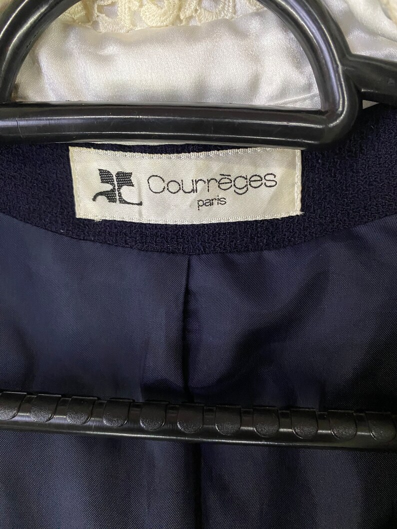 Puede incluir: Una etiqueta blanca con texto negro que dice "Courr&egrave;ges Paris" sobre un fondo de tela azul marino.