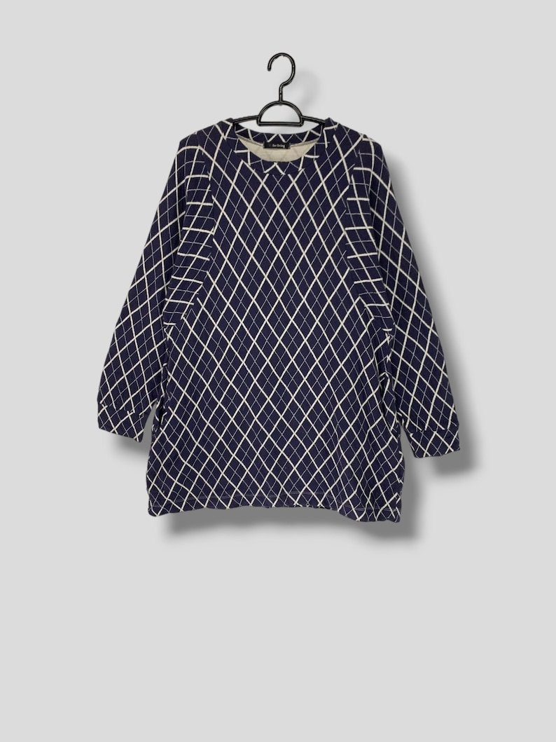 May include: A navy blue long-sleeved top with a white diamond pattern. The top is hanging on a black hanger. The garment has a crew neck and a relaxed fit, suitable for casual wear.