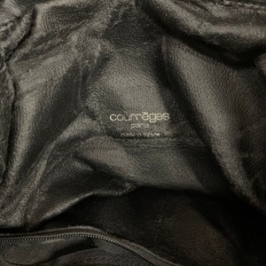 May include: Close-up of the interior of a black leather handbag. The bag features a textured surface and a label with the text "courr&egrave;ges paris made in france" in a silver font.