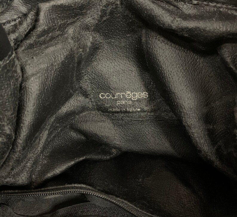 May include: Close-up of the interior of a black leather handbag. The bag features a textured surface and a label with the text "courr&egrave;ges paris made in france" in a silver font.