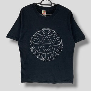 Op de afbeelding: Zwart T-shirt met een wit geometrisch sfeerontwerp. De afbeelding bestaat uit onderling verbonden driehoeken, waardoor een driedimensionaal effect ontstaat. Het shirt hangt aan een zwarte hanger tegen een lichtgrijze achtergrond.