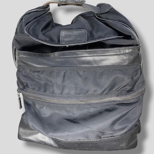 May include: Black shoulder bag with a curved design. The bag features a top handle, a zippered compartment, and leather accents. The bag is made of a nylon material and has a leather base.