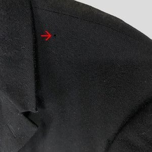 May include: Close-up of a black wool jacket with a seam detail on the shoulder. The seam is stitched with a straight stitch and has a small hole in the fabric.