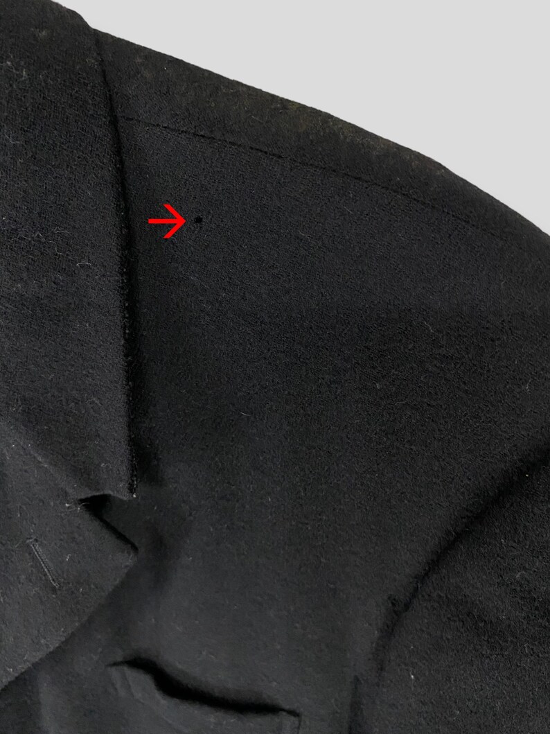 May include: Close-up of a black wool jacket with a seam detail on the shoulder. The seam is stitched with a straight stitch and has a small hole in the fabric.