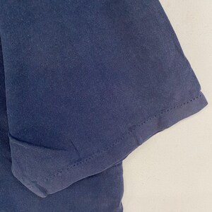 May include: Close-up of a navy blue t-shirt sleeve. The fabric is a solid color with a visible seam at the hem of the sleeve. The sleeve is slightly folded, showing the inside of the fabric.