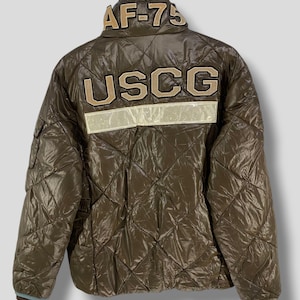 May include: Brown quilted jacket with the text "AF-75" on the collar and "USCG" across the back. The jacket has a reflective white stripe and a light blue trim.