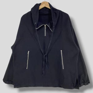Könnte beinhalten: Schwarze Jacke mit hohem Kragen und silbernem Reißverschluss. Die Jacke hat zwei Seitentaschen mit silbernen Reißverschlüssen und einen Kordelzug am Ausschnitt. Die Jacke hängt an einem Holzbügel.