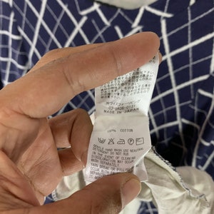 May include: Navy blue and white patterned long-sleeve shirt. The shirt has a grid-like design. The tag reads "100% Cotton" and includes care instructions. The shirt is made in Japan.