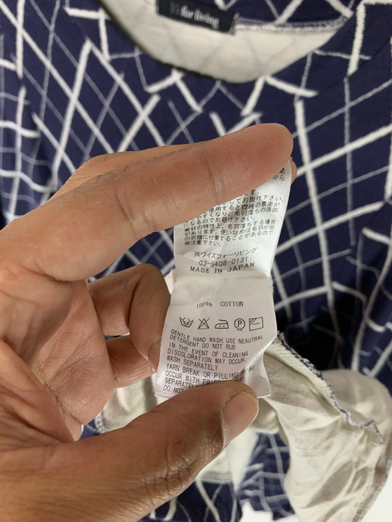 May include: Navy blue and white patterned long-sleeve shirt. The shirt has a grid-like design. The tag reads "100% Cotton" and includes care instructions. The shirt is made in Japan.