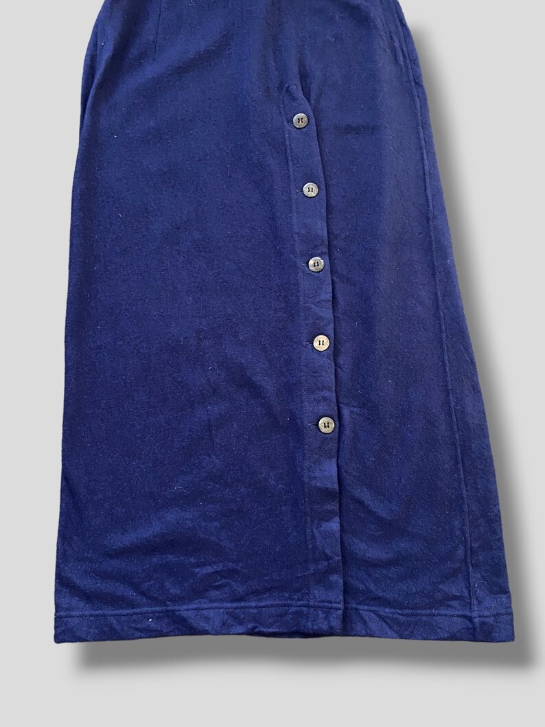 Puede incluir: Una falda azul marino con botones en la parte delantera. La falda est&aacute; hecha de una tela suave y tiene siete botones en el lateral. La falda es de color liso y tiene un dise&ntilde;o sencillo y cl&aacute;sico.