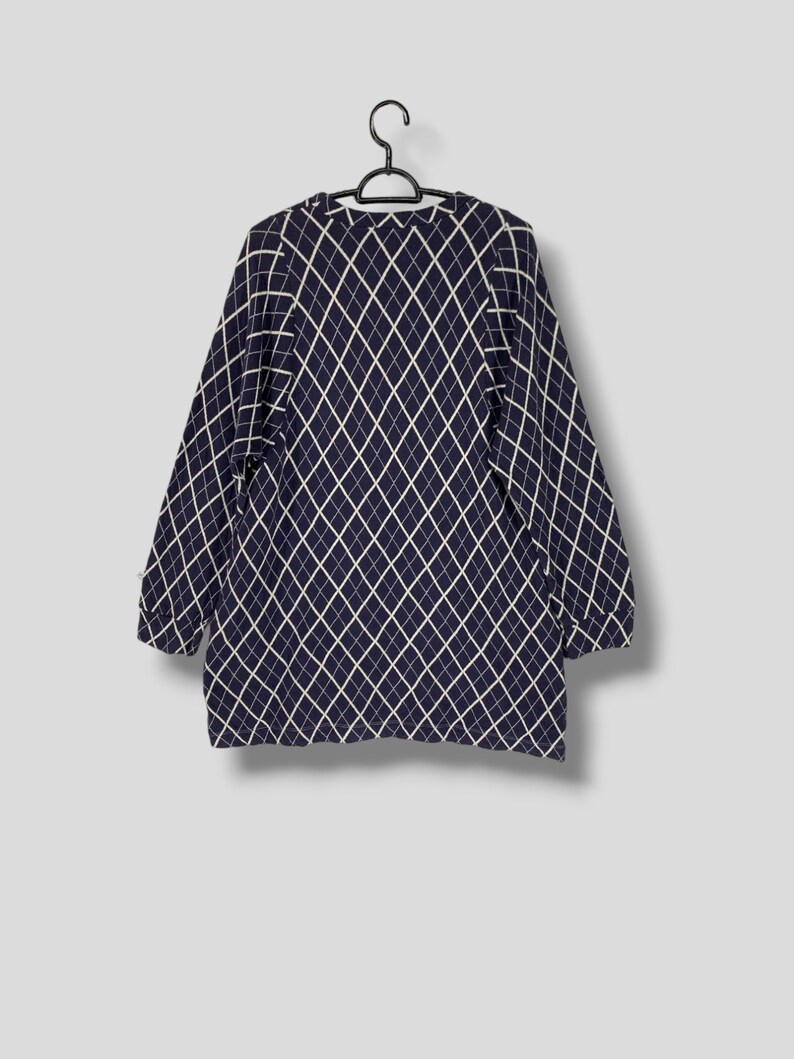 May include: Navy blue long-sleeve sweater with a white diamond pattern. The sweater is hanging on a black hanger against a light gray background. The sweater has a crew neck and long sleeves.