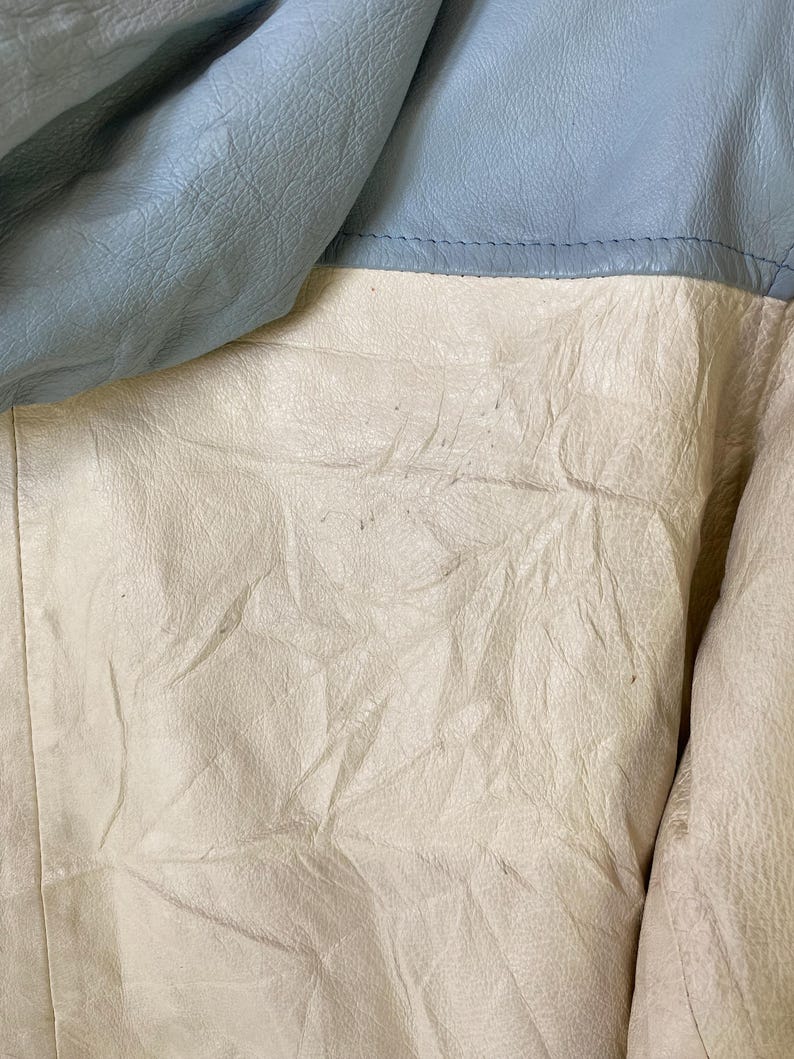 Puede incluir: Primer plano de una chaqueta de cuero azul claro y blanco roto. La chaqueta est&aacute; hecha de cuero suave y flexible y tiene una superficie texturizada.