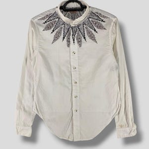 Puede incluir: Una camisa blanca de manga larga con botones y un patrón geométrico negro y marrón alrededor del cuello.