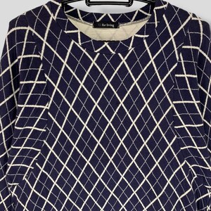 May include: A navy blue long-sleeve shirt with a white diamond pattern. The shirt has a crew neck and the text "V for living" is visible on the inside collar. The shirt is hanging on a black hanger.