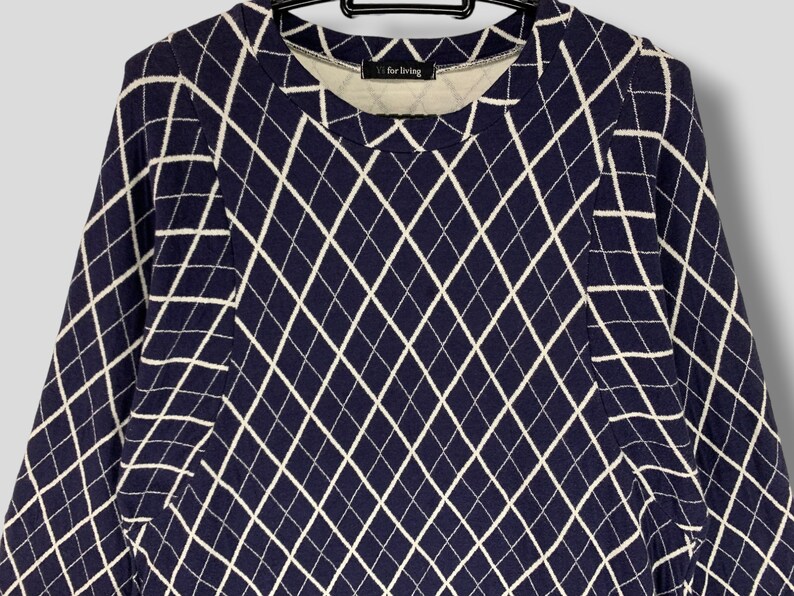 May include: A navy blue long-sleeve shirt with a white diamond pattern. The shirt has a crew neck and the text "V for living" is visible on the inside collar. The shirt is hanging on a black hanger.