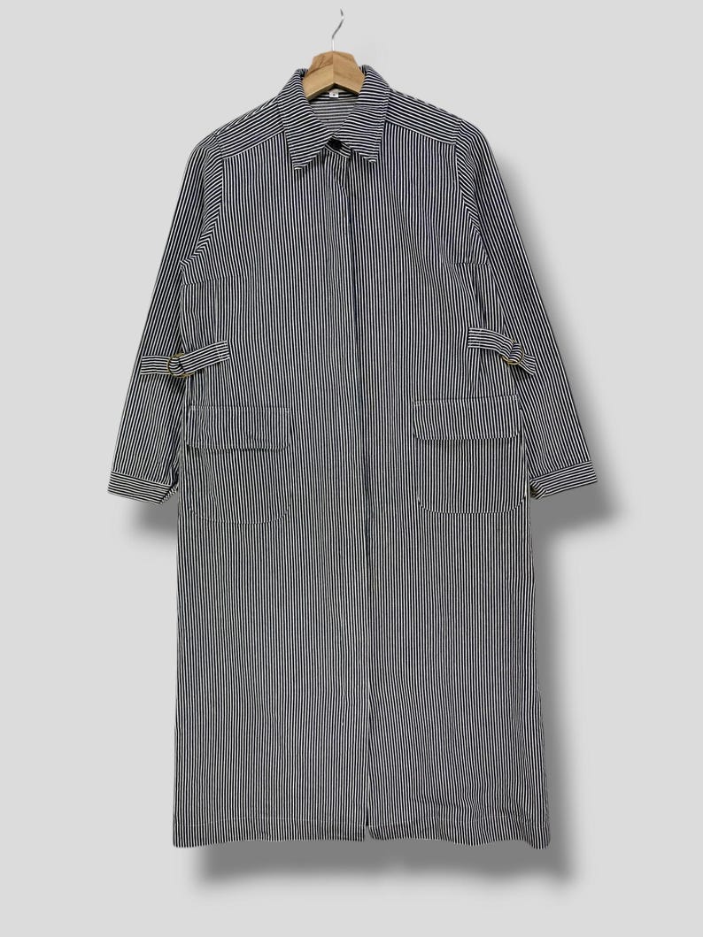 May include: A long, striped, black and white, collared shirt with a zipper closure and two pockets. The shirt has straps on the sleeves.