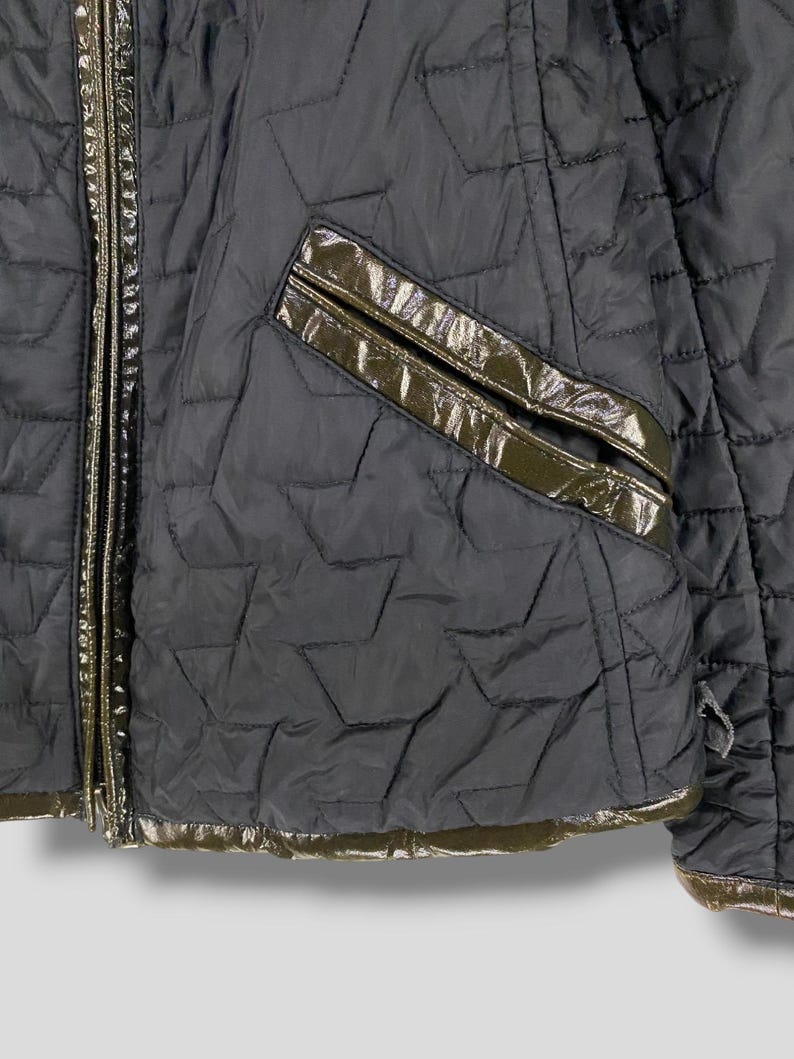 May include: A black quilted jacket with a zipper closure and a brown leather trim. The jacket has a pocket on the left side and a quilted pattern.