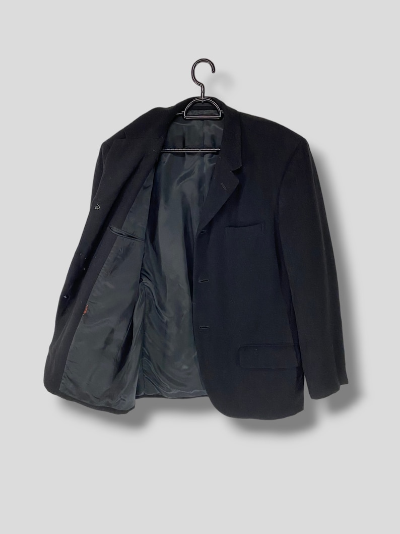 May include: A black blazer with a single button closure and two pockets. The blazer is hanging on a black hanger.