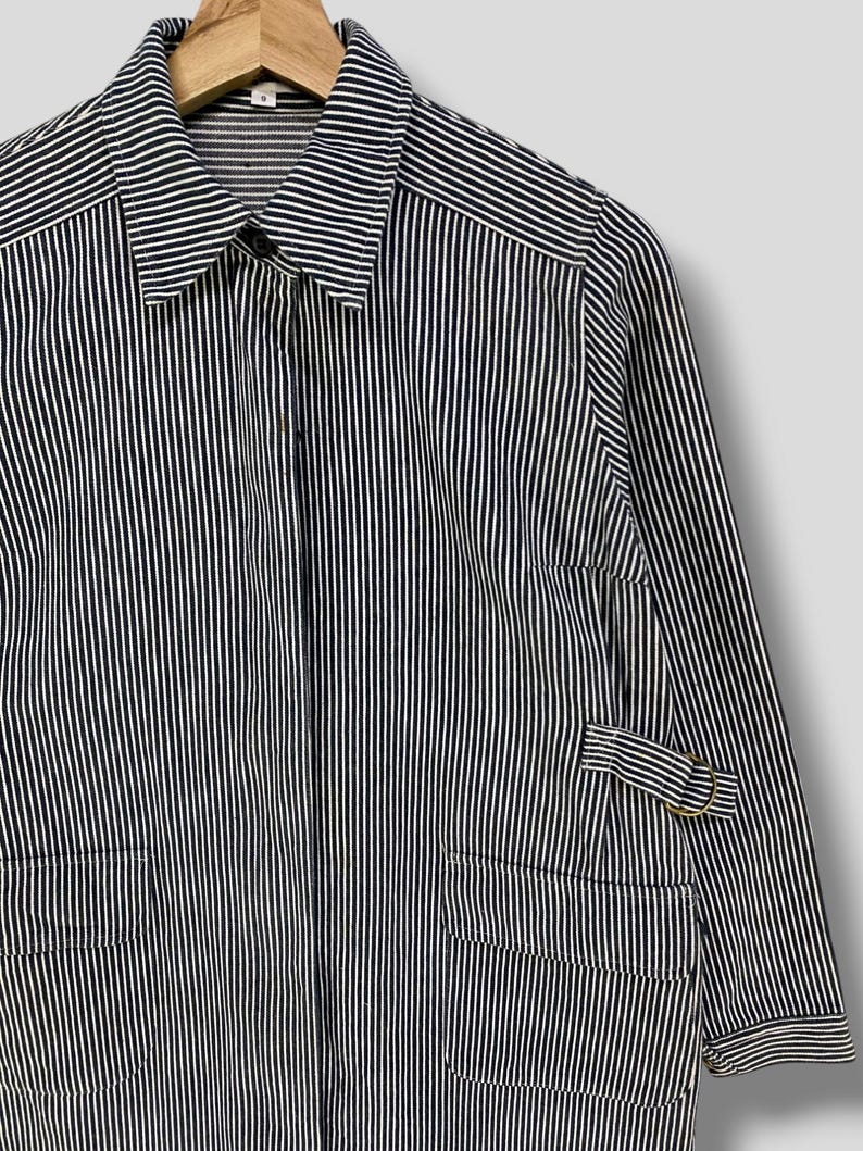 May include: A long-sleeved, striped shirt with a button-up collar and a single pocket on the left side. The shirt is made of a lightweight fabric and has a relaxed fit.