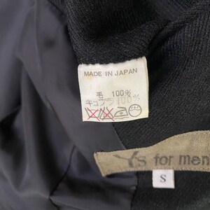 May include: A black blazer with a label that reads "MADE IN JAPAN" and "毛 100% キュプラ 100%". The label also has a care tag with a dry clean symbol and a medium heat iron symbol. The blazer has a label that reads "Y's for men" and "S" for the size.